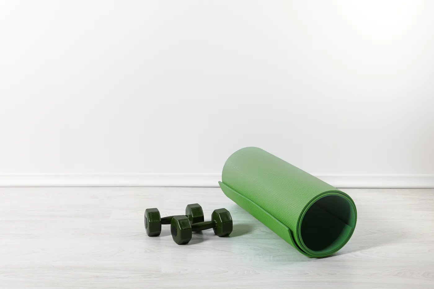 Grüne Gymnastikmatte und zwei kleine Hanteln auf hellem Holzboden